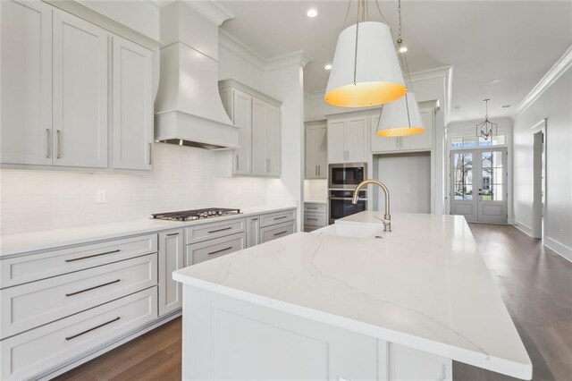 kitchen with decorative light fixtures, white cabinetry, light stone countertops, stainless steel appliances, and custom range hood