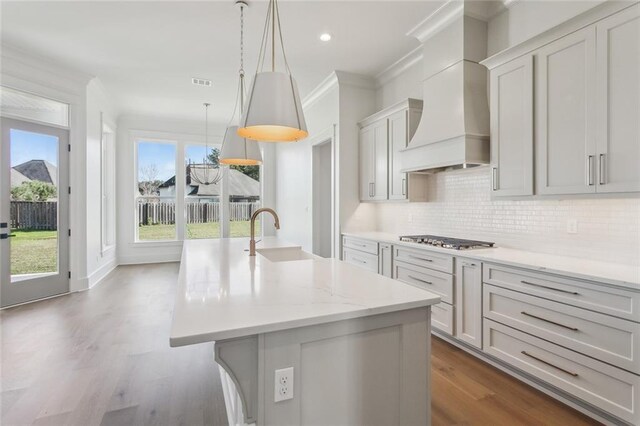 kitchen with stainless steel gas stovetop, white cabinetry, custom exhaust hood, backsplash, and light wood-type flooring