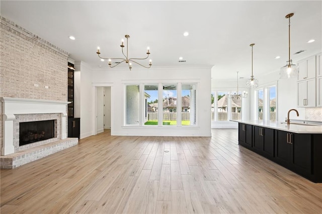 unfurnished living room with sink, light hardwood / wood-style floors, a brick fireplace, brick wall, and a notable chandelier