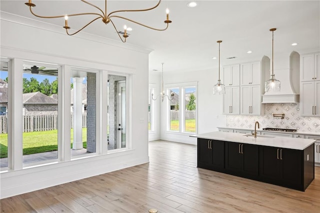 kitchen featuring extractor fan, white cabinets, an island with sink, light wood-type flooring, and backsplash