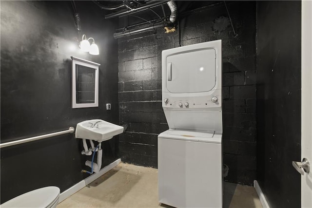 bathroom with stacked washing maching and dryer, sink, concrete flooring, and toilet