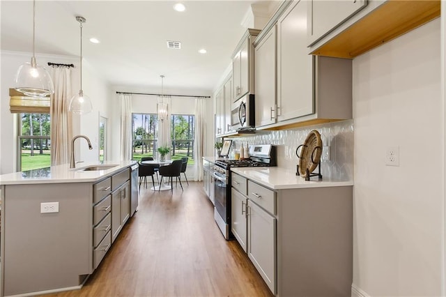 kitchen with a center island with sink, gray cabinets, stainless steel appliances, tasteful backsplash, and decorative light fixtures