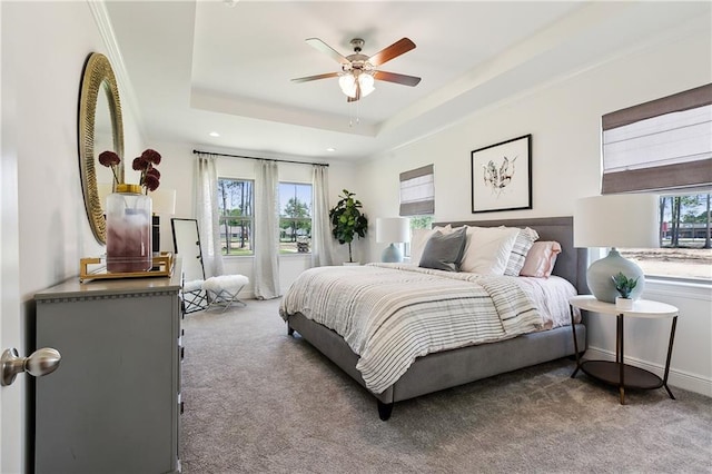 bedroom featuring ceiling fan, light colored carpet, a tray ceiling, and multiple windows