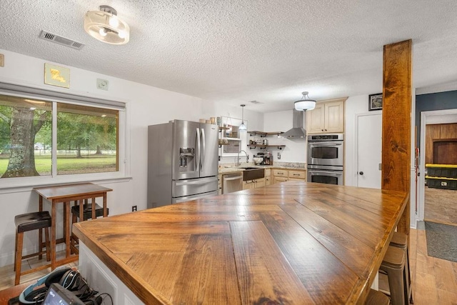 kitchen with pendant lighting, sink, light hardwood / wood-style floors, stainless steel appliances, and wall chimney range hood