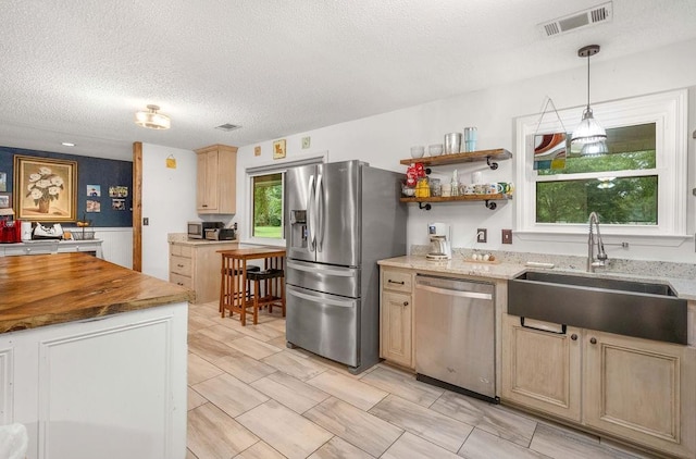 kitchen featuring pendant lighting, sink, butcher block counters, stainless steel appliances, and a textured ceiling