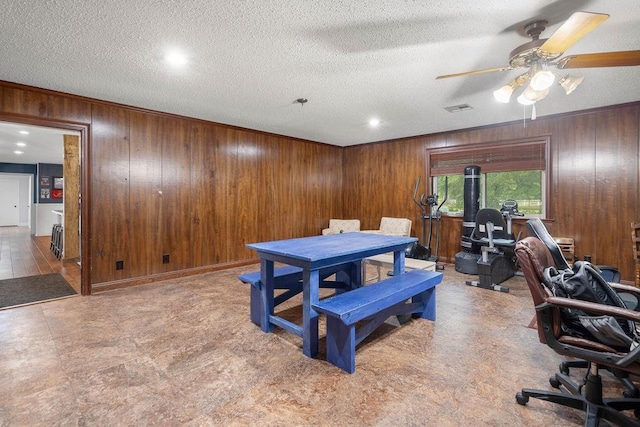 dining room featuring ceiling fan, wooden walls, and a textured ceiling