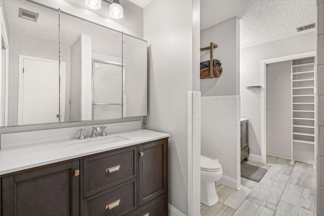 bathroom featuring walk in shower, vanity, toilet, and a textured ceiling