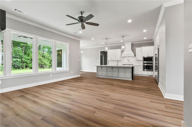 kitchen featuring premium range hood, a kitchen island with sink, light wood-type flooring, and built in appliances