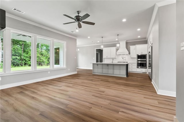 kitchen with stainless steel microwave, decorative light fixtures, an island with sink, white cabinets, and custom range hood