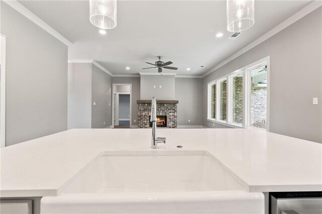 kitchen featuring a fireplace, ceiling fan, ornamental molding, sink, and a kitchen island with sink