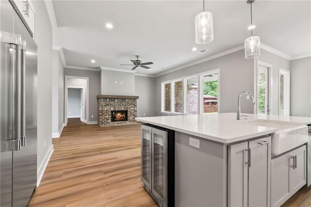 kitchen with high quality fridge, pendant lighting, a fireplace, an island with sink, and wine cooler