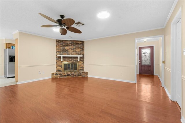 unfurnished living room featuring a fireplace, ceiling fan, brick wall, hardwood / wood-style flooring, and ornamental molding