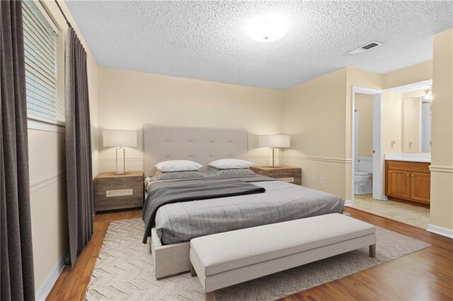 bedroom with ensuite bath, a textured ceiling, and light hardwood / wood-style floors