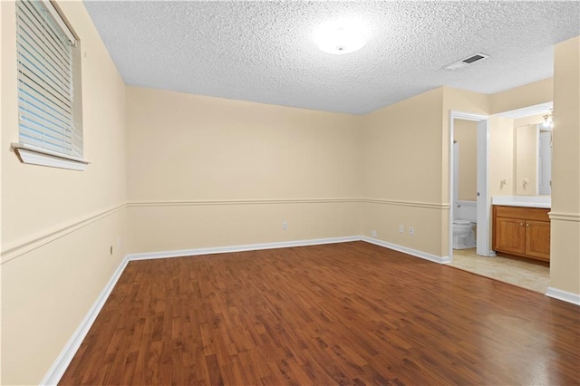 unfurnished bedroom with ensuite bathroom, a textured ceiling, and wood-type flooring