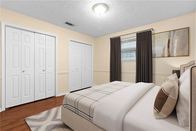 bedroom featuring two closets, a textured ceiling, and wood-type flooring