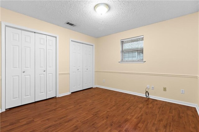 unfurnished bedroom with multiple closets, a textured ceiling, and hardwood / wood-style floors