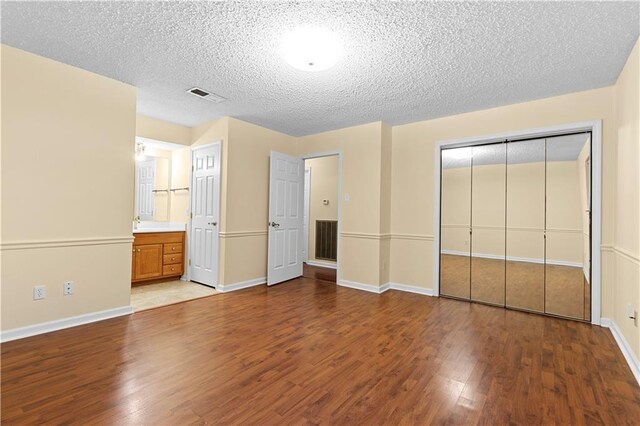 unfurnished bedroom with hardwood / wood-style flooring, a closet, ensuite bath, and a textured ceiling