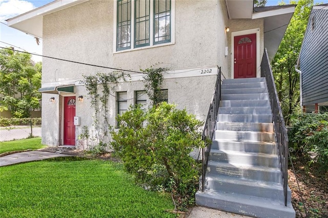 entrance to property featuring a yard, fence, and stucco siding