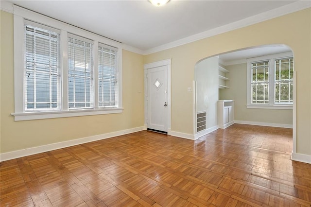 foyer entrance featuring arched walkways, crown molding, and baseboards