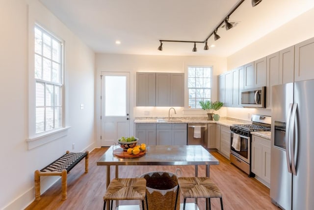 kitchen with appliances with stainless steel finishes, sink, gray cabinetry, light hardwood / wood-style floors, and light stone countertops