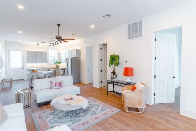 living room featuring ceiling fan, sink, and light wood-type flooring