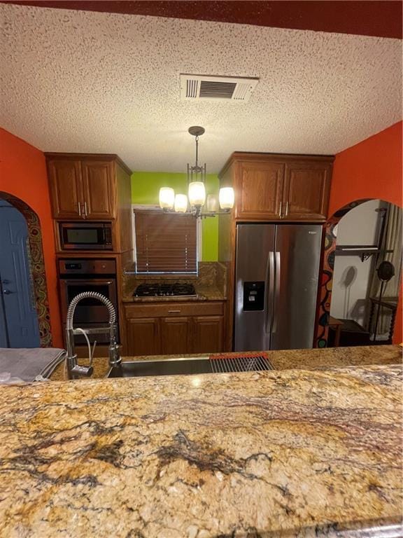 kitchen with appliances with stainless steel finishes, decorative light fixtures, a textured ceiling, and a notable chandelier