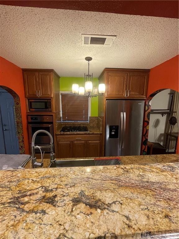 kitchen featuring appliances with stainless steel finishes, an inviting chandelier, a textured ceiling, and decorative light fixtures