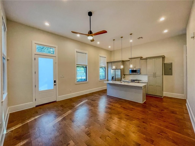 kitchen featuring appliances with stainless steel finishes, a center island with sink, hanging light fixtures, dark hardwood / wood-style flooring, and ceiling fan