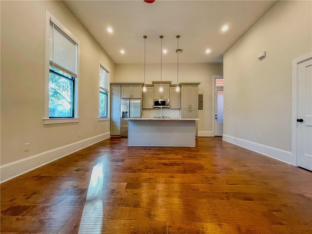 kitchen featuring dark hardwood / wood-style flooring, gray cabinets, appliances with stainless steel finishes, decorative light fixtures, and a center island with sink