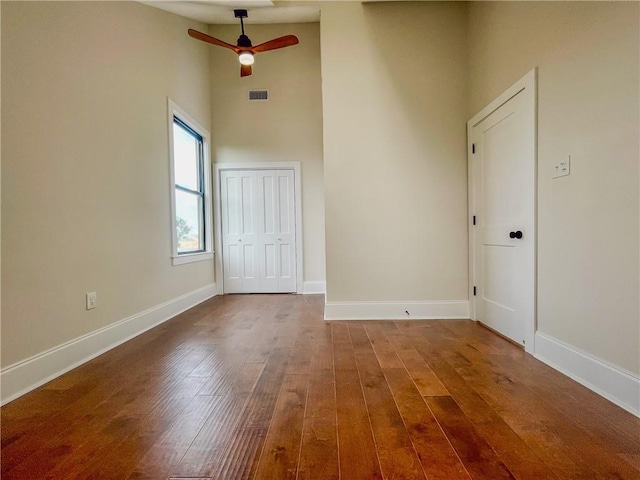 spare room with a high ceiling, wood-type flooring, visible vents, and baseboards