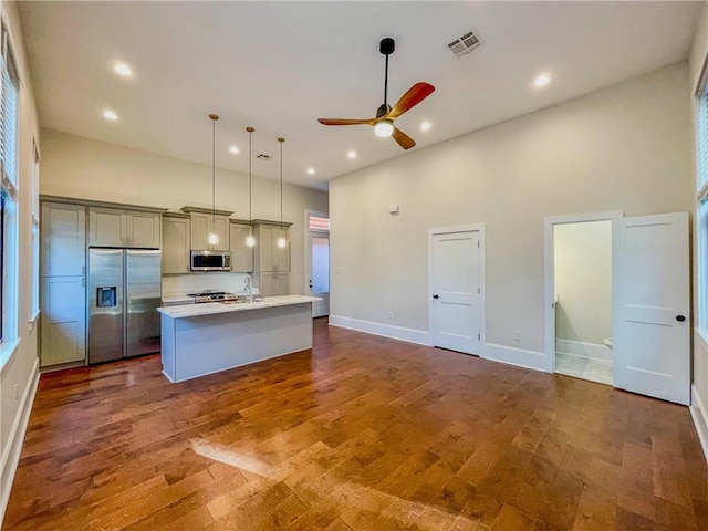 kitchen with appliances with stainless steel finishes, pendant lighting, an island with sink, ceiling fan, and wood-type flooring