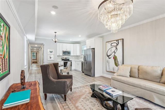 living room with an inviting chandelier, ornamental molding, and light hardwood / wood-style floors