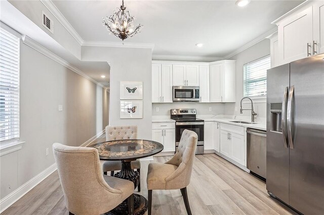 kitchen with white cabinetry, light hardwood / wood-style flooring, appliances with stainless steel finishes, sink, and ornamental molding