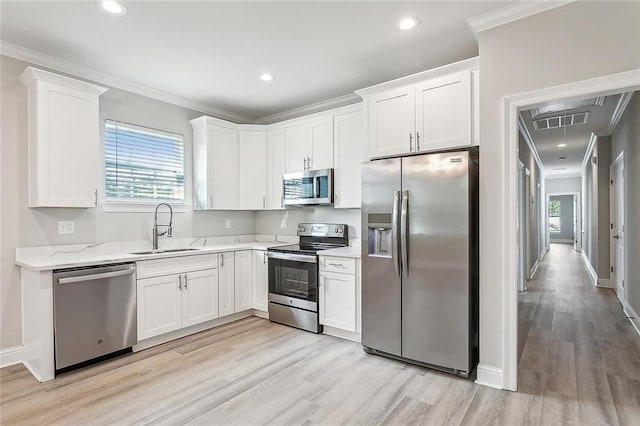 kitchen featuring light wood-type flooring, white cabinets, appliances with stainless steel finishes, sink, and ornamental molding