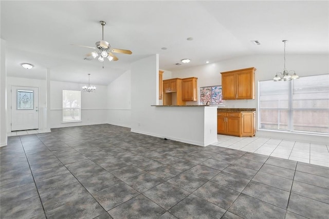 unfurnished living room with ceiling fan with notable chandelier, dark tile patterned floors, lofted ceiling, and a wealth of natural light