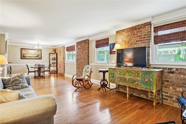 living area with baseboards, brick wall, ornamental molding, wood finished floors, and an inviting chandelier