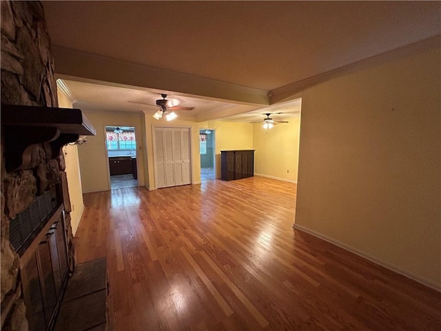 unfurnished living room with a stone fireplace, ceiling fan, hardwood / wood-style floors, and beamed ceiling