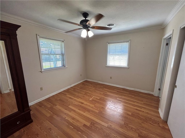 unfurnished bedroom with hardwood / wood-style floors, multiple windows, ornamental molding, and ceiling fan