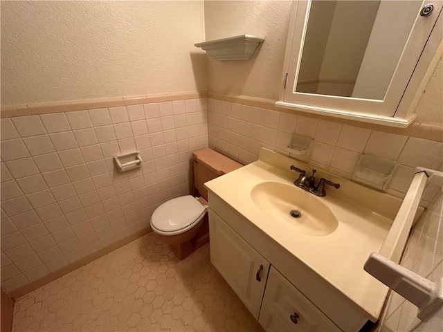 bathroom with tile patterned floors, vanity, tile walls, and toilet