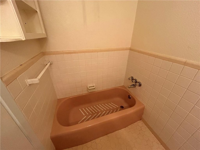 bathroom with tile patterned flooring, a bath, and tile walls