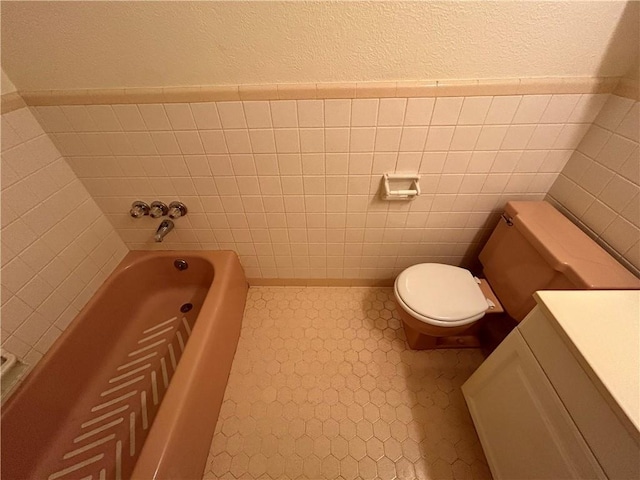 bathroom featuring vanity, toilet, a tub, and tile walls