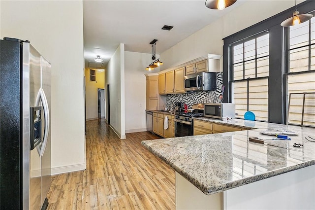 kitchen with hanging light fixtures, kitchen peninsula, stainless steel appliances, light wood-type flooring, and stone counters