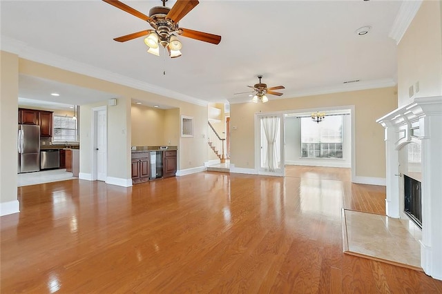 unfurnished living room featuring ornamental molding, ceiling fan, light wood-type flooring, and a high end fireplace