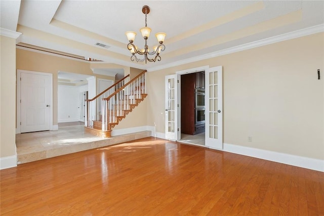 spare room with light hardwood / wood-style floors, ornamental molding, a chandelier, and a tray ceiling