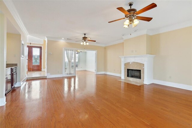 unfurnished living room with a fireplace, wood-type flooring, ceiling fan, and crown molding