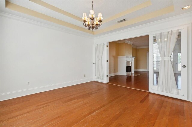 unfurnished room with a high end fireplace, an inviting chandelier, a raised ceiling, and hardwood / wood-style floors