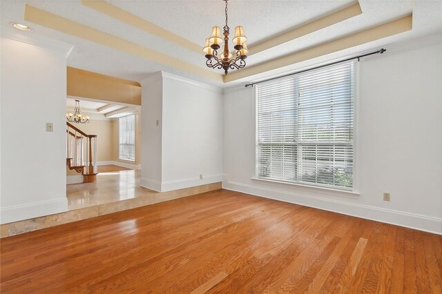 empty room with a chandelier, light hardwood / wood-style flooring, and a raised ceiling