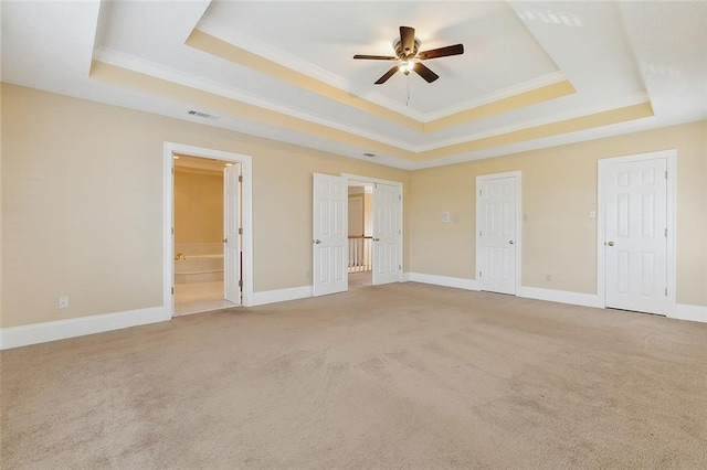 unfurnished bedroom featuring connected bathroom, a raised ceiling, light carpet, and ceiling fan