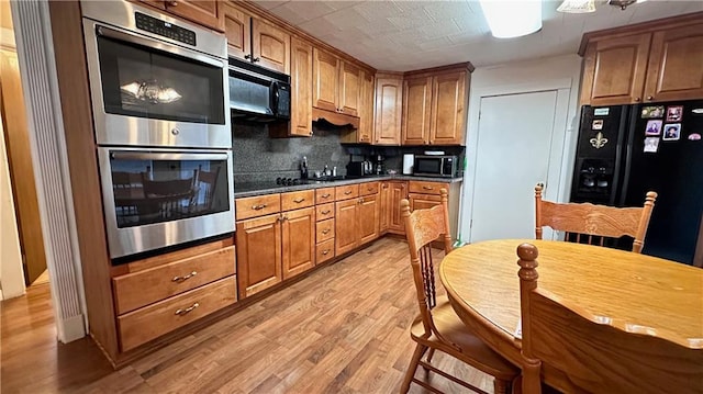 kitchen featuring light wood-type flooring, black appliances, sink, and tasteful backsplash