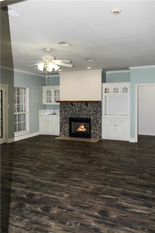 unfurnished living room with a premium fireplace, ornamental molding, dark wood-type flooring, and ceiling fan